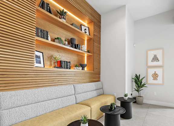 A living room with a yellow couch, a wooden shelf with books and plants, and a painting on the wall.