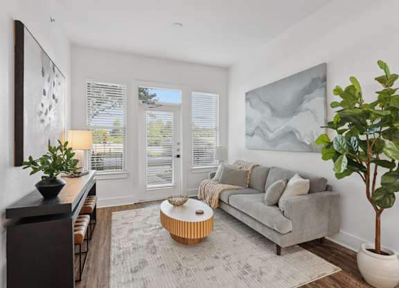 A living room with a grey couch, a coffee table, a potted plant, and a painting on the wall.