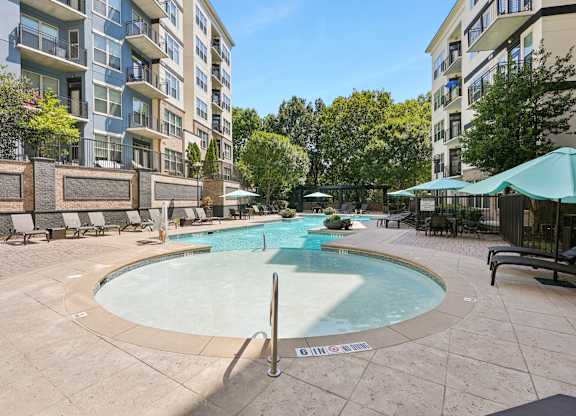 A large outdoor swimming pool surrounded by a stone wall and lounge chairs.