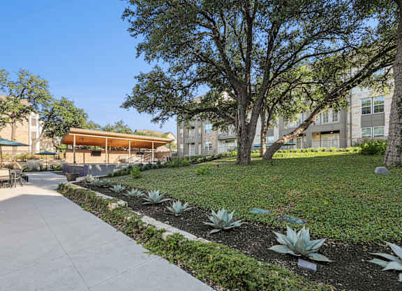 A concrete walkway leads through a landscaped area with a building in the background.