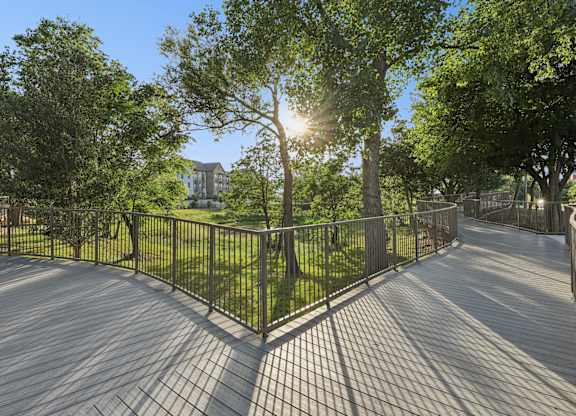 A sunny day at the park with a wooden walkway and metal fence.