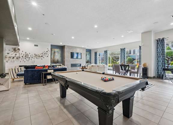 A pool table is in the middle of a room with a blue sofa and a painting on the wall.