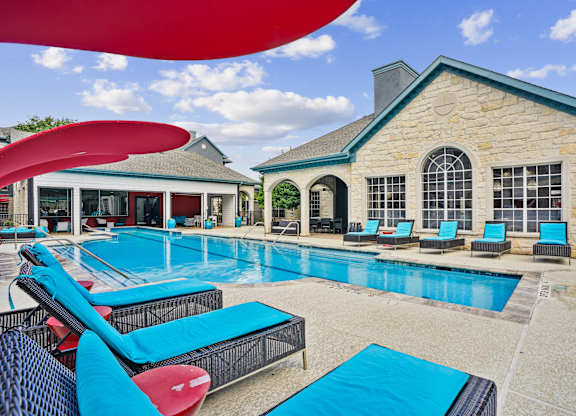 A large swimming pool with lounge chairs and a building in the background.