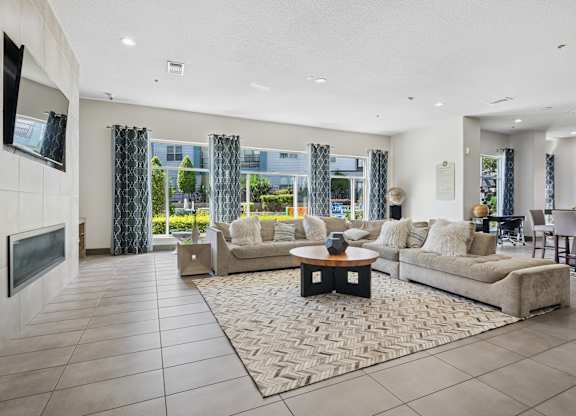 A modern living room with a large couch, a coffee table, and a flat-screen TV mounted on the wall.