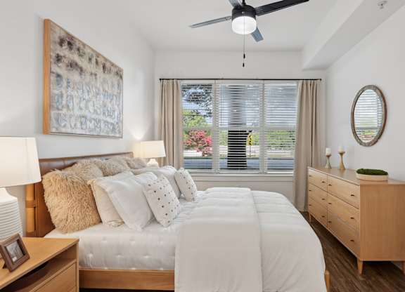 A bedroom with a large bed, a ceiling fan, and a painting on the wall.