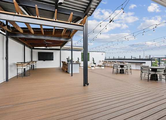 A wooden deck with tables and chairs and string lights.