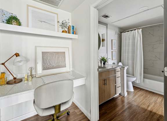 A white chair is in front of a desk with a lamp and picture frame on it.