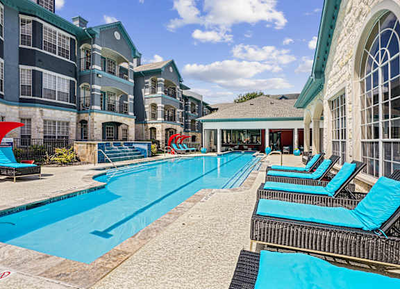 A large swimming pool with lounge chairs and a building in the background.