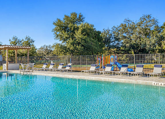 A pool with chairs and a pergola in the background.