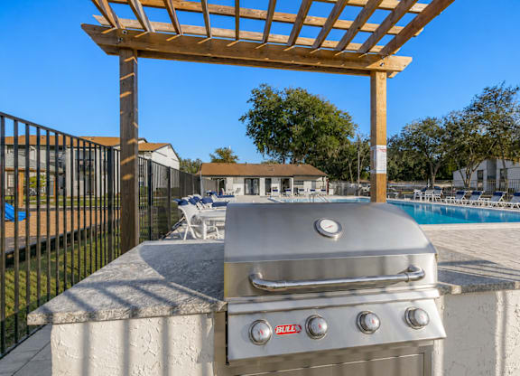 A BBQ grill is on a concrete slab with a pergola above it.