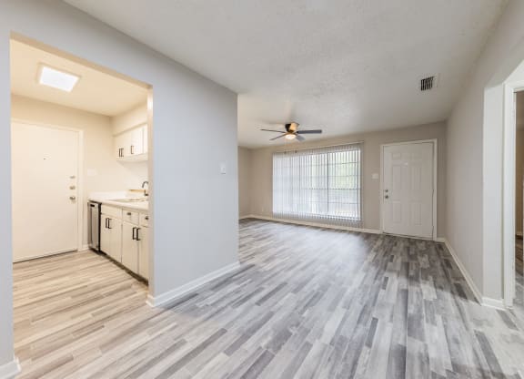 an empty living room with a ceiling fan and a kitchen in the background