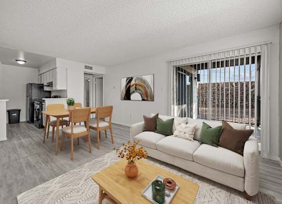 A living room with a white couch, a wooden coffee table, and a dining table with chairs.