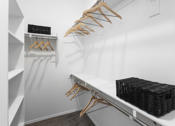 a walk in closet with a white wall and a shelf with wicker baskets