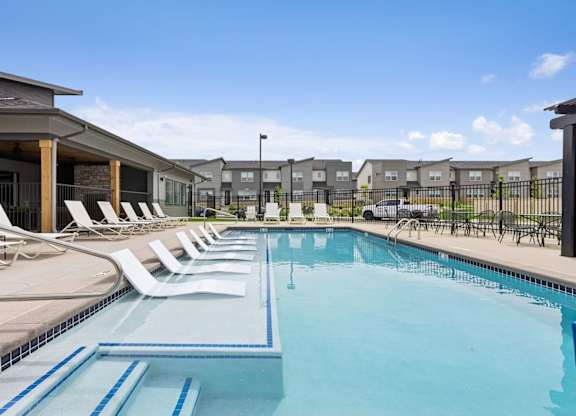 A swimming pool with lounge chairs and a fence in the background.