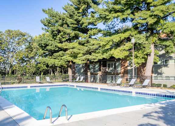A swimming pool surrounded by trees and chairs.