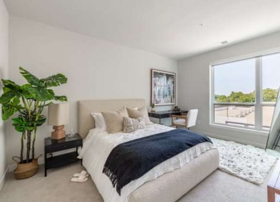 A bedroom with a large bed and a view of the outdoors through a large window.
