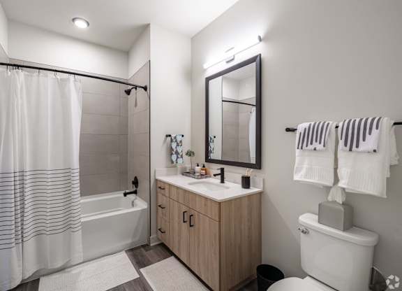 A modern bathroom with a white toilet, a white sink, a white shower curtain, and a wooden cabinet.