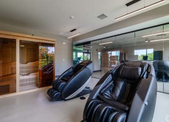 Two black leather recliner chairs are in a spacious room with a glass wall and a wooden door.