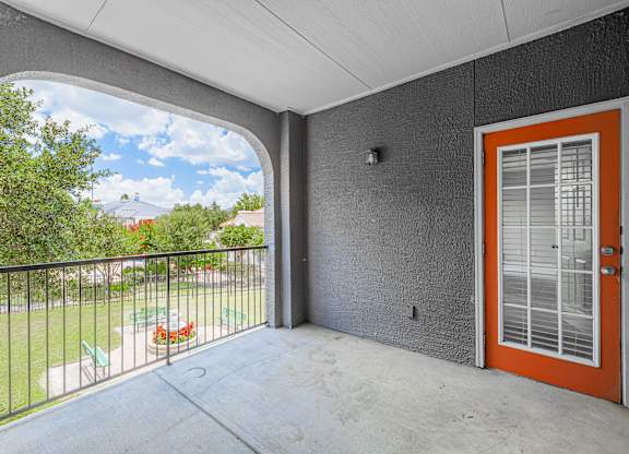 A balcony with a red door and a view of a green lawn and trees.