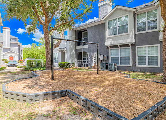 A tree stands in a sandbox in front of a grey apartment.