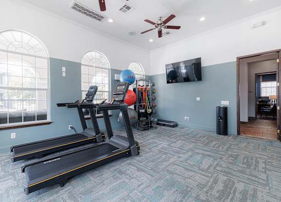 A treadmill and exercise equipment are in a spacious room with a ceiling fan.