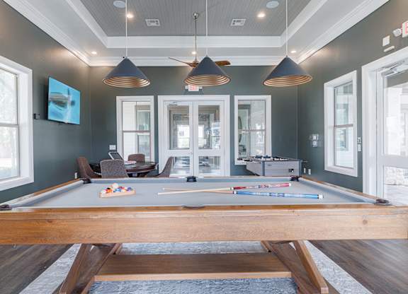 A pool table is in the middle of a room with a wooden floor and a ceiling fan.