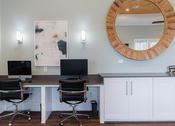 Two computers are on a desk with a mirror and two lights above.