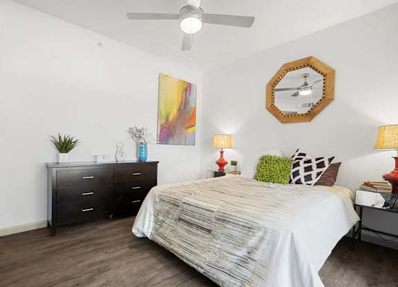 A bedroom with a bed, dresser, and ceiling fan.