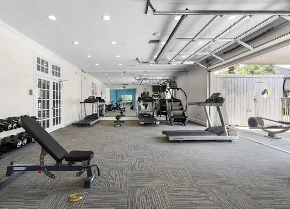 A gym with a variety of equipment including a treadmill, weights, and a bench press.