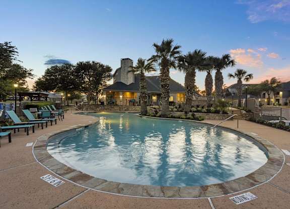 A large outdoor swimming pool surrounded by palm trees and lounge chairs.