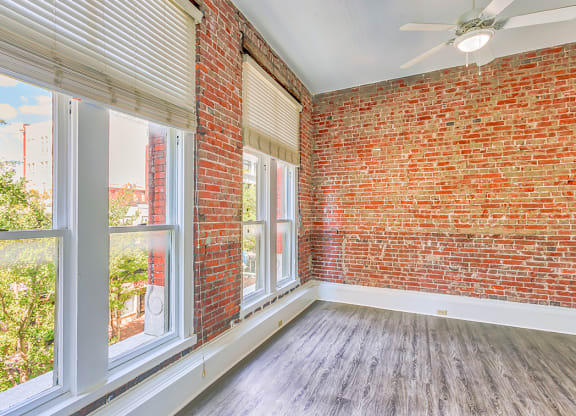 an empty room with large windows and a red brick wall