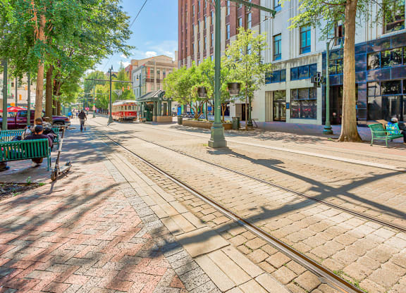 a city street with streetcar tracks and people sitting on benches