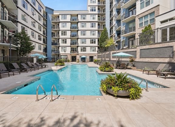 A swimming pool surrounded by lounge chairs and planters in a courtyard.