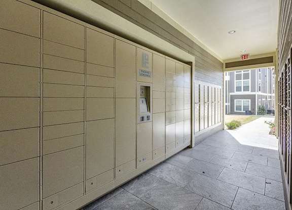 A long hallway with a wall of lockers and a red exit sign at the end.
