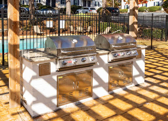 two bbq grills on a patio with a pool in the background