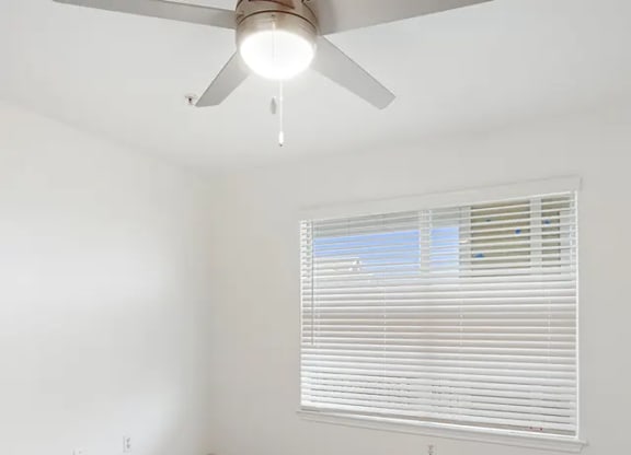 A room with a ceiling fan and a window with blinds.