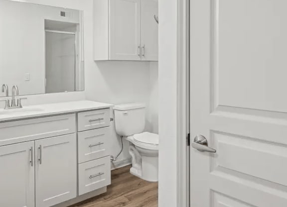A white bathroom with a toilet, sink, and cabinets.