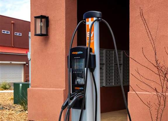 An electric vehicle charging station is installed on a sidewalk outside a building.