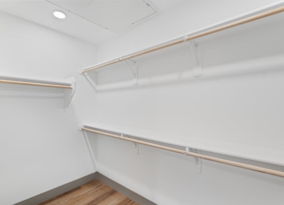 a walk in closet with white walls and a wood floor