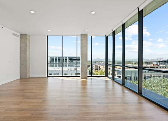 A large empty room with wooden floors and a view of the city through large windows.