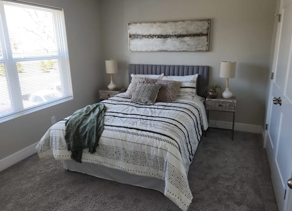 A bedroom with a bed, two lamps, and a painting on the wall.
