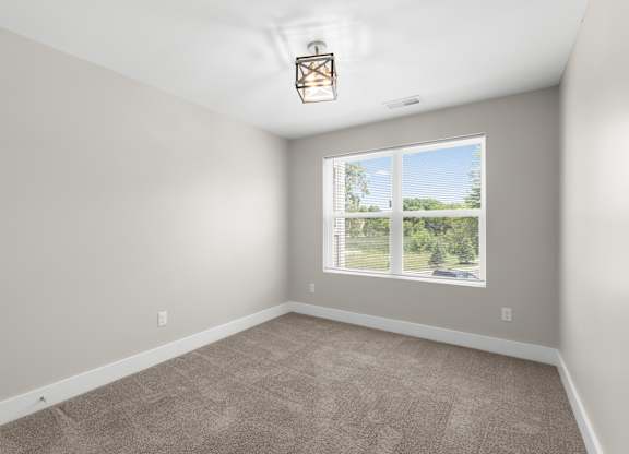 A room with a carpeted floor and a window showing a view of trees and a house.