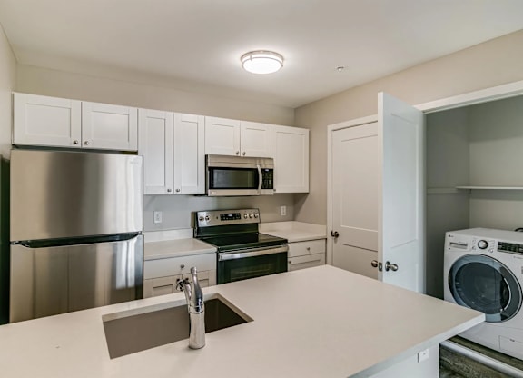 A kitchen with a refrigerator, microwave, oven, and washing machine.