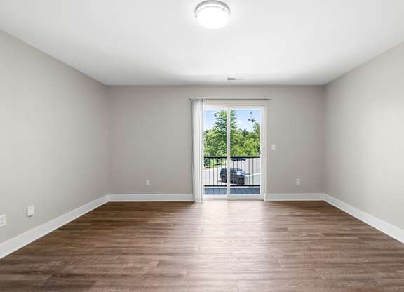 A room with wooden floors and a sliding glass door leading to a balcony.