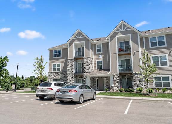 Two cars are parked in a parking lot in front of a large apartment building.