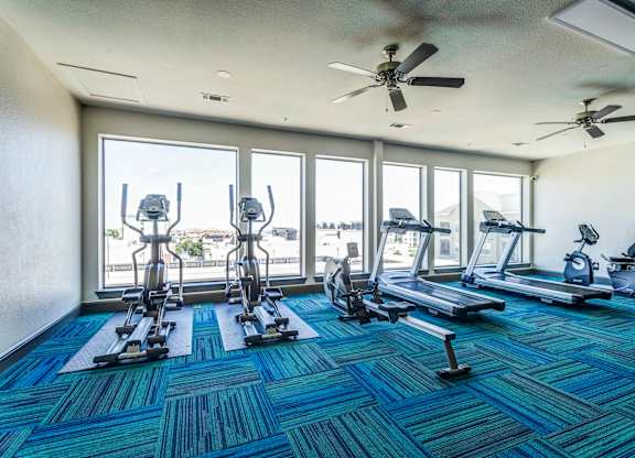 a gym with cardio equipment and large windows with a view of the water