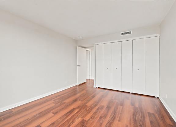 A room with wooden floors and white walls with a row of white cupboards.
