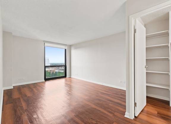 A bedroom with wooden floors and floor to ceiling windows and spacious closet.
