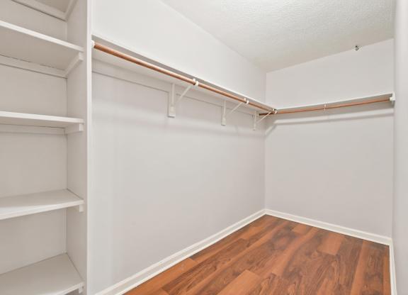 A white closet with shelves and a wood floor.