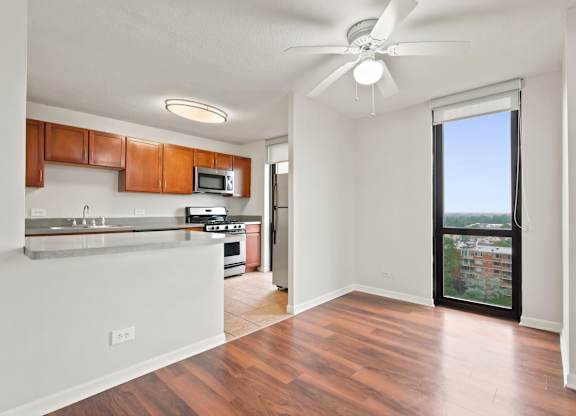 A dining room with ceiling fan and floor to ceiling window with the kitchen in the background.